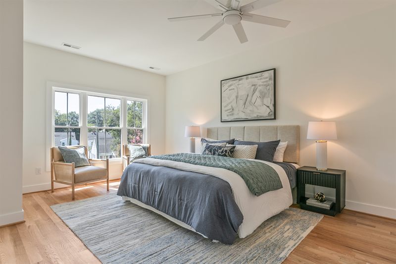 Staged bedroom with an upholstered headboard, layered bedding and two chairs by the window