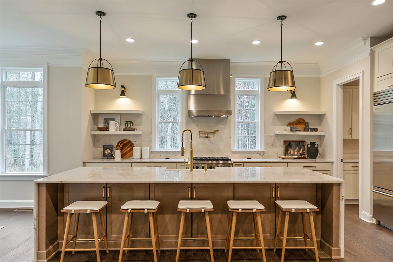 Staged kitchen with a marble island, five counter stools and three lantern pendants