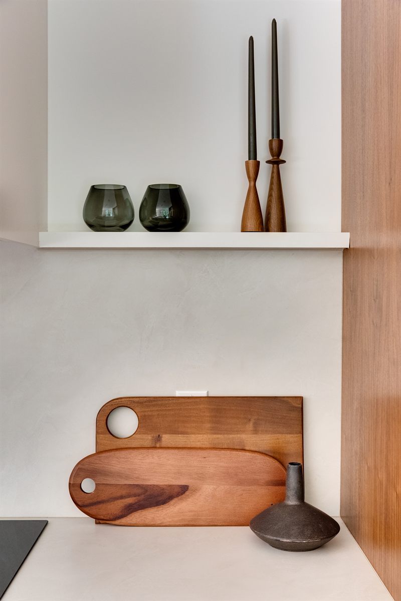 Smoked glass tumblers and turned wood candlesticks on a floating shelf above two cutting boards
