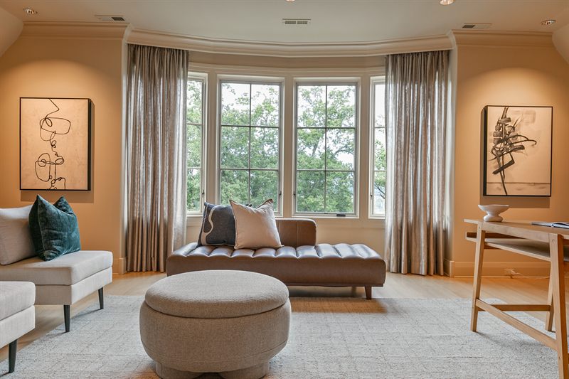 Sitting room with a leather chaise in a bay window, a round ottoman and two line-drawing prints