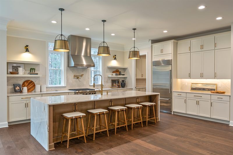 Kitchen with a marble island, five wood and brass counter stools and lantern pendants overhead