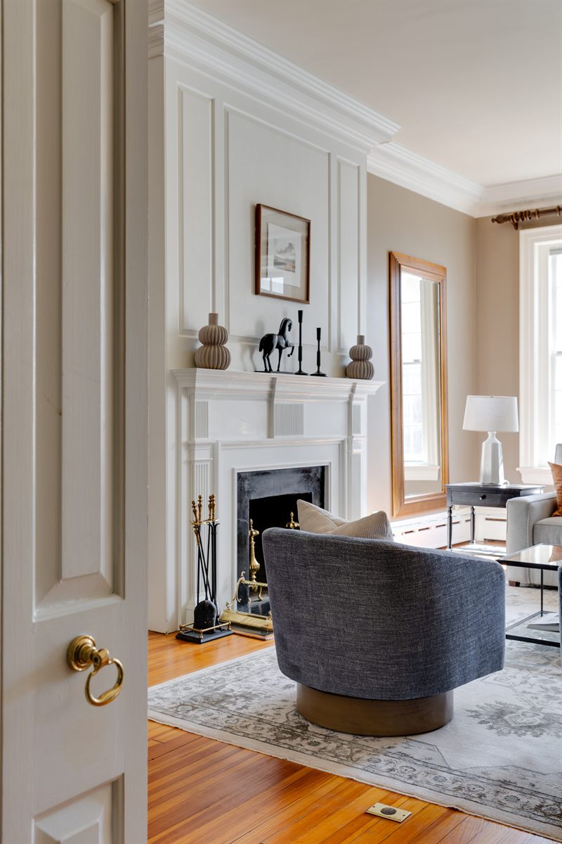 Living room fireplace with an ornate white mantel and a grey swivel chair on a patterned rug