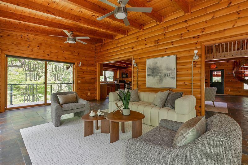 Log-walled living room with a cream sofa, boucle chairs and doors onto a deck above the water