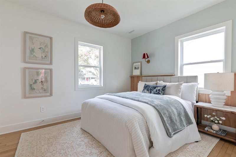 Bedroom with pale blue walls, a woven pendant, wood headboard and two framed botanical prints