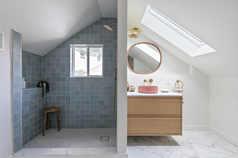 Bathroom with a blue tiled walk-in shower, skylight, oak floating vanity and a pink basin