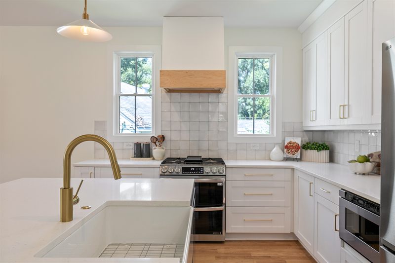 White kitchen with a brass faucet, farmhouse sink, gas range and square tile backsplash